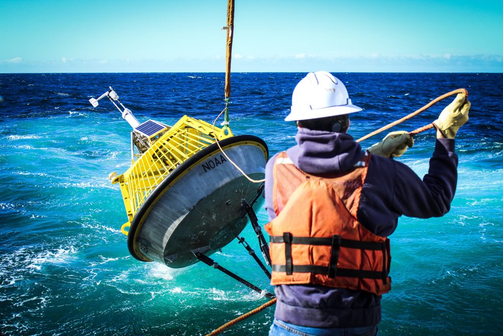 scientist in orange vest pulling on a yellow ocean bouy